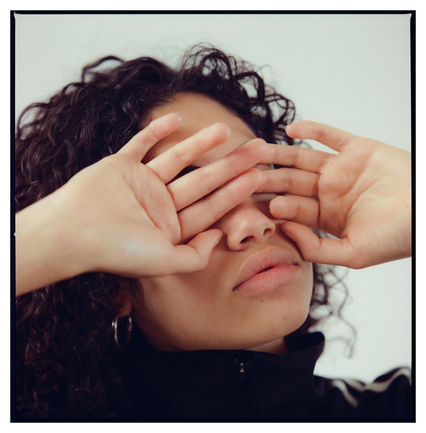 A woman with curly hair covers her eyes with her hands.