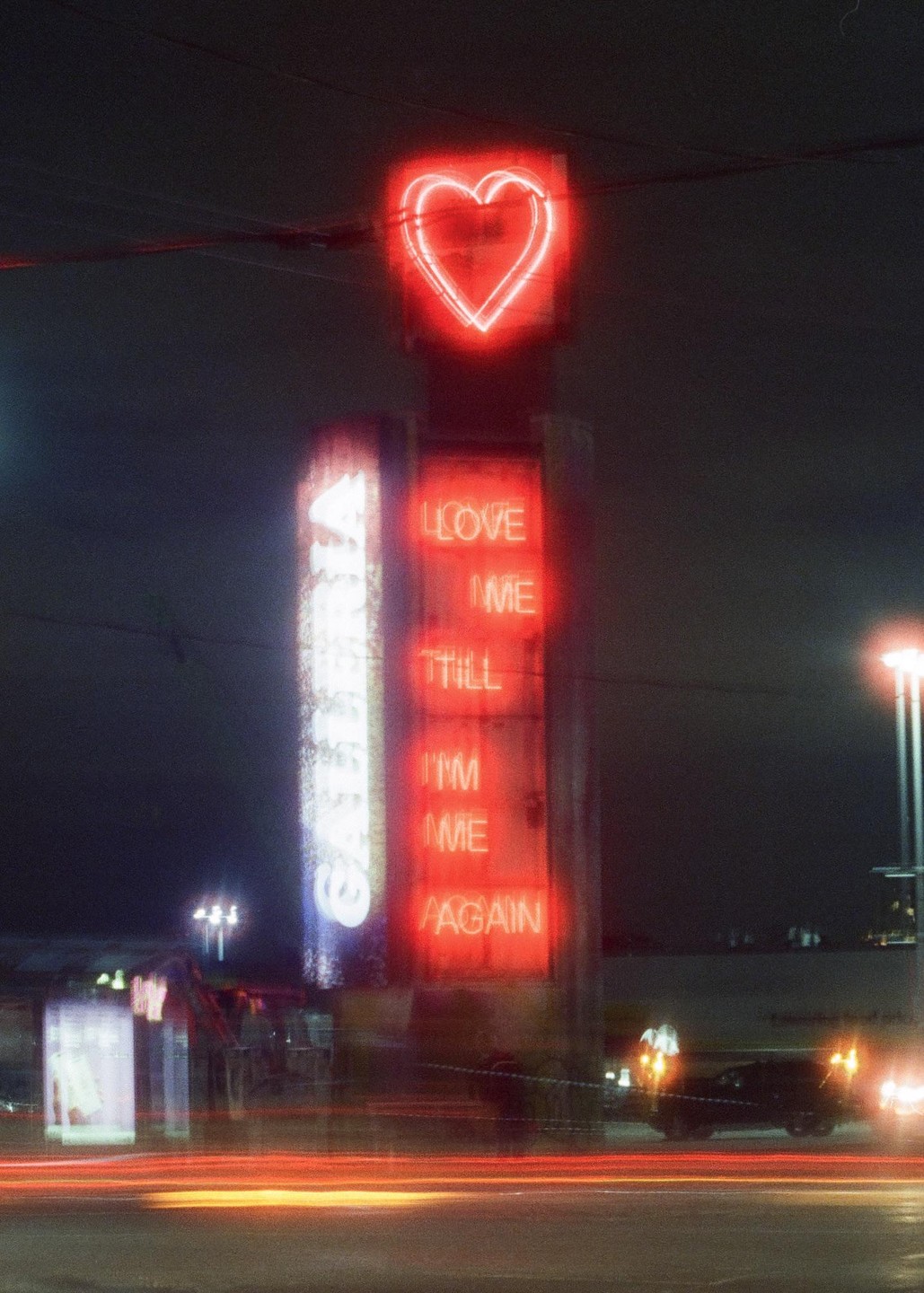 A red neon heart and text sign are visible at night with light trails from vehicles on the street.