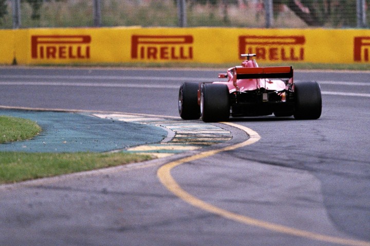A red formula one race car speeds around a track with a yellow barrier in the background.
