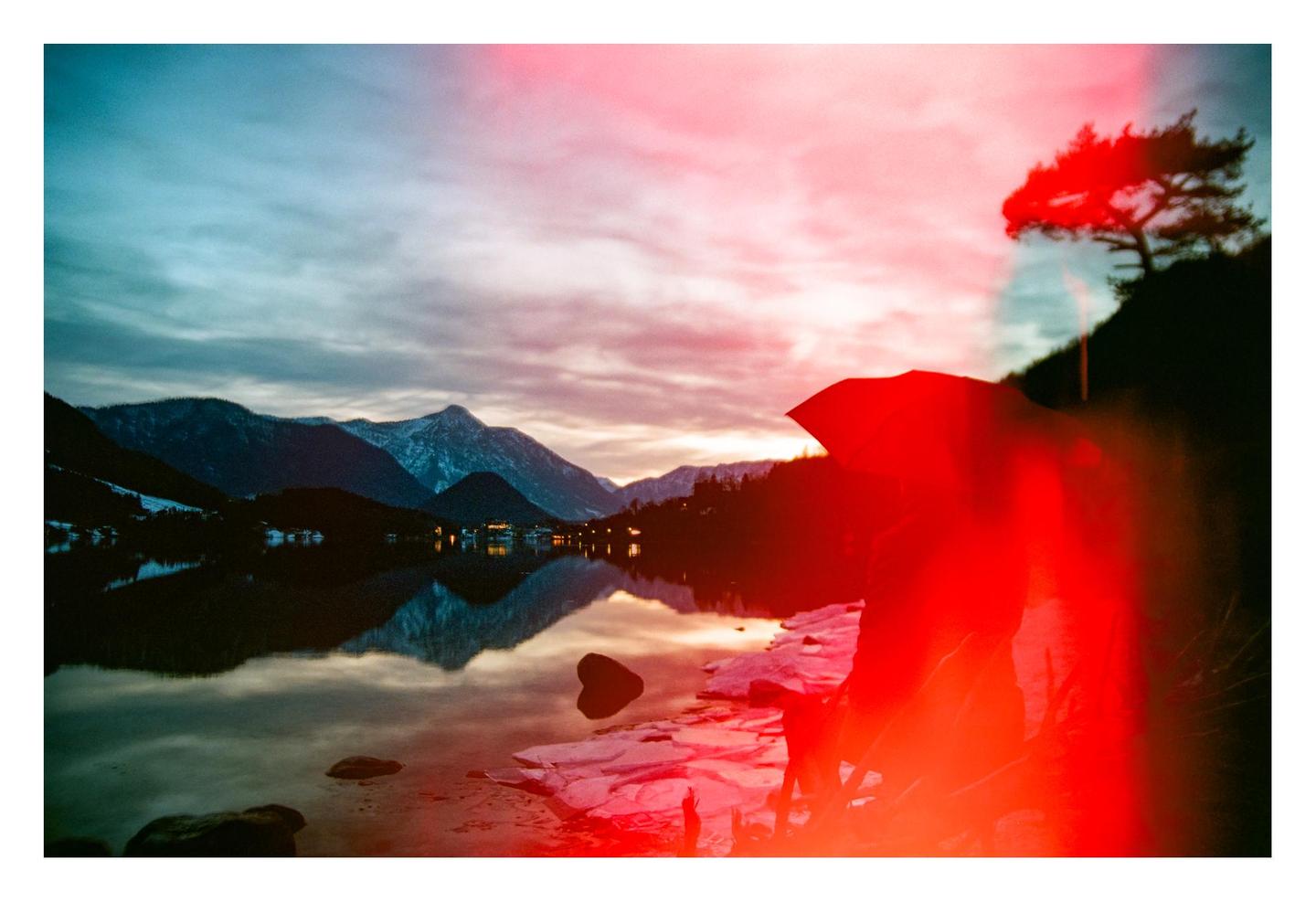 A red light leak covers the right side of a landscape photograph of a lake surrounded by mountains and a small town.