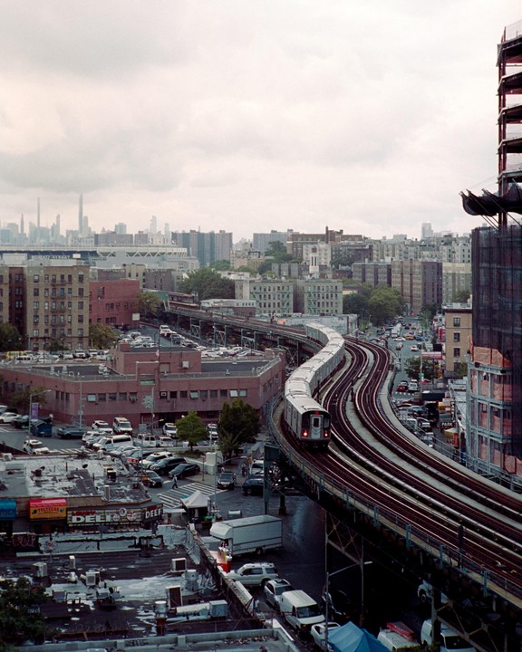A train travels on an elevated track through a city with many buildings and cars.
