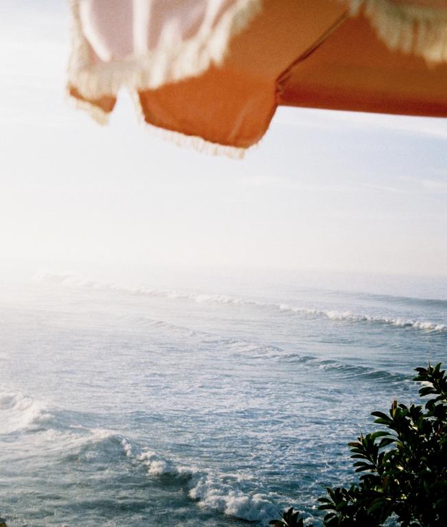 A parasol is visible in the upper part of the frame, with the ocean and some foliage below.