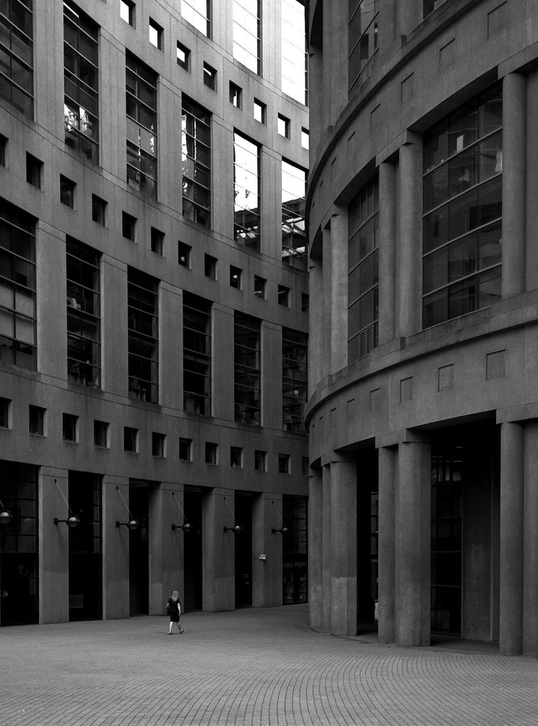 A person walks across a paved courtyard surrounded by tall, modern buildings with many windows.