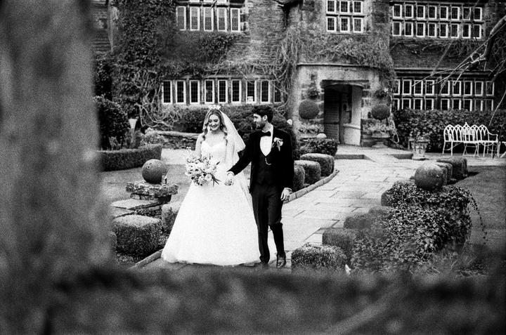 A couple walks hand in hand along a stone path in front of a large building with many windows.