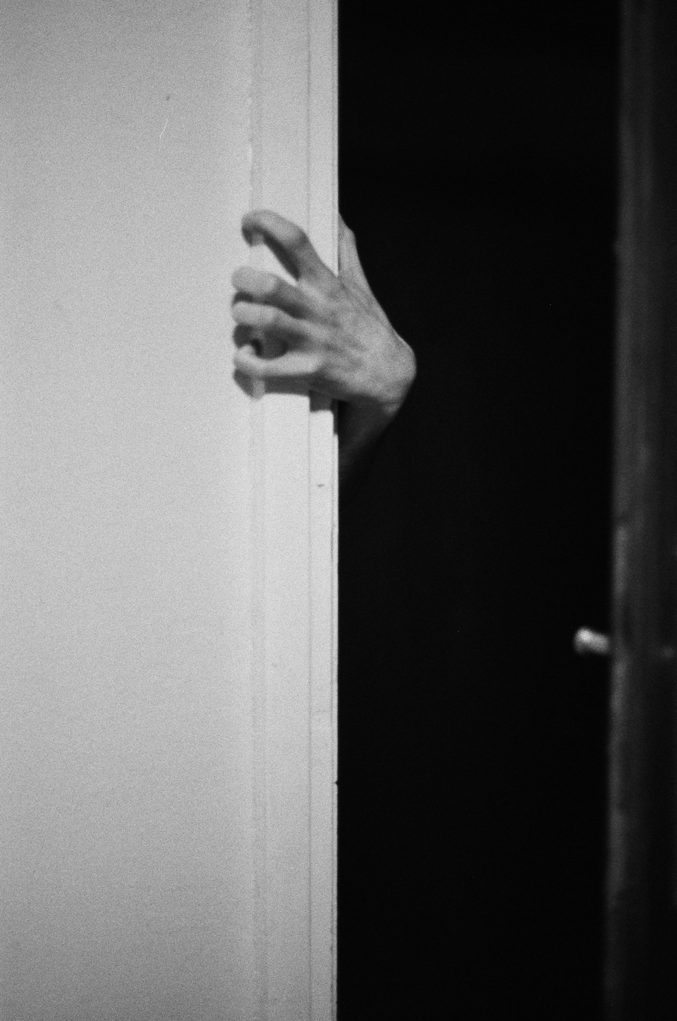 A hand is visible in the dark, holding onto the edge of a door frame.