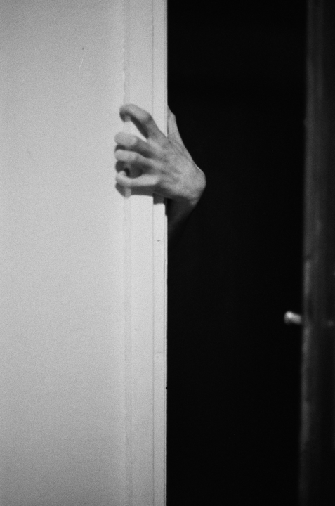 A hand is visible in the dark, holding onto the edge of a door frame.