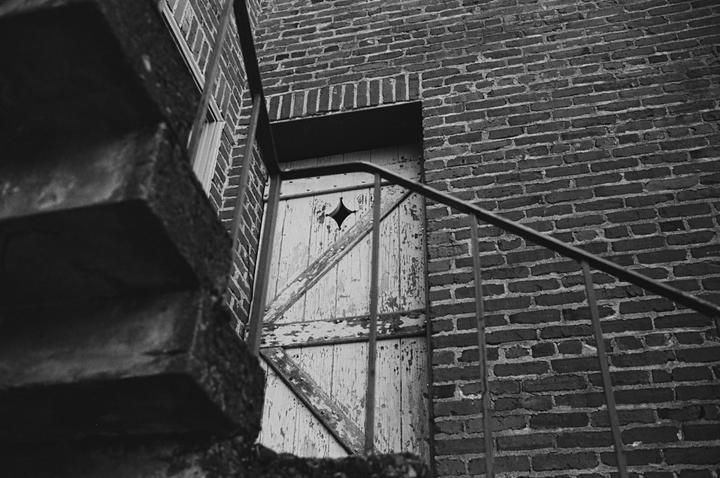 A weathered wooden door with a star-shaped cutout is visible behind a metal railing and brick wall.