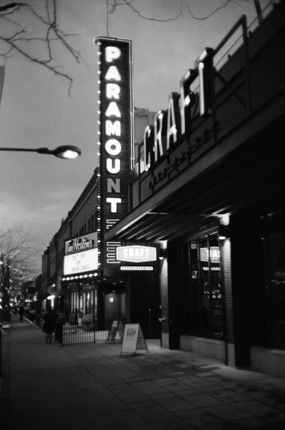A street at night is lined with buildings featuring illuminated signs, including one for "Paramount" and another for "Tim Hortons."
