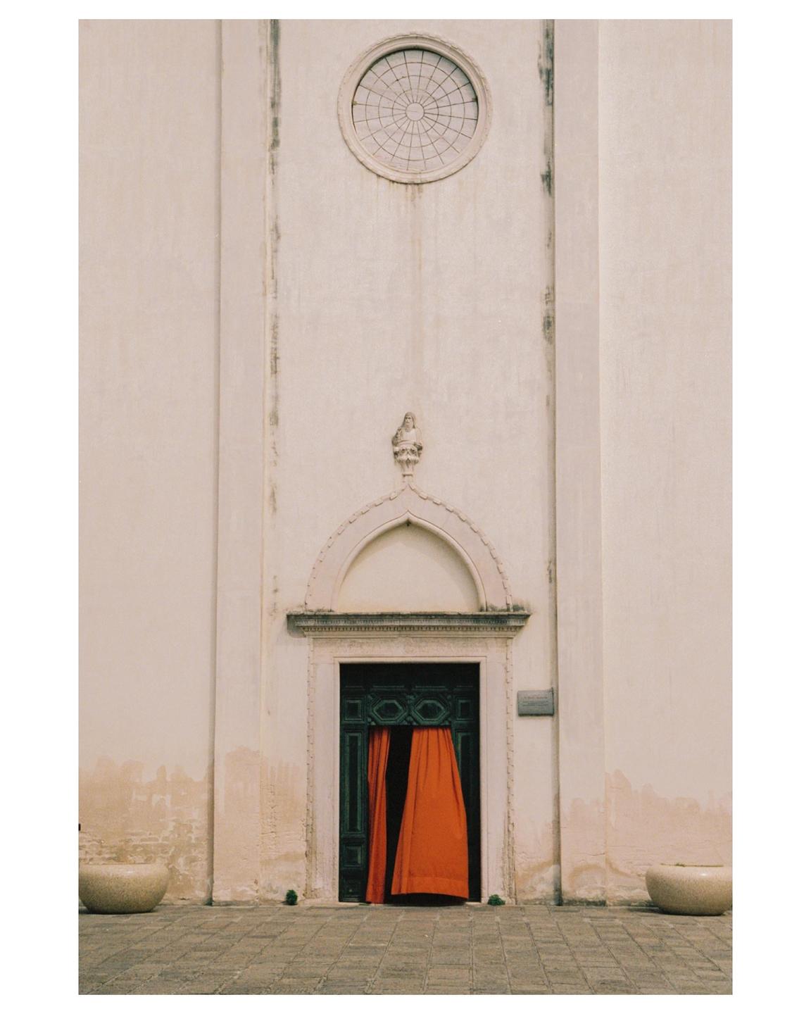 A building with a dark green door and bright orange curtains is visible from a low angle.