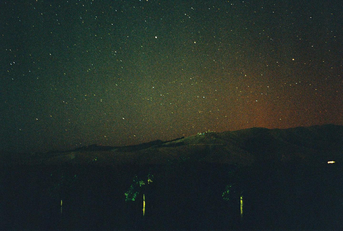 A starry night sky with a faint aurora glow is visible above a dark landscape with hills and trees.