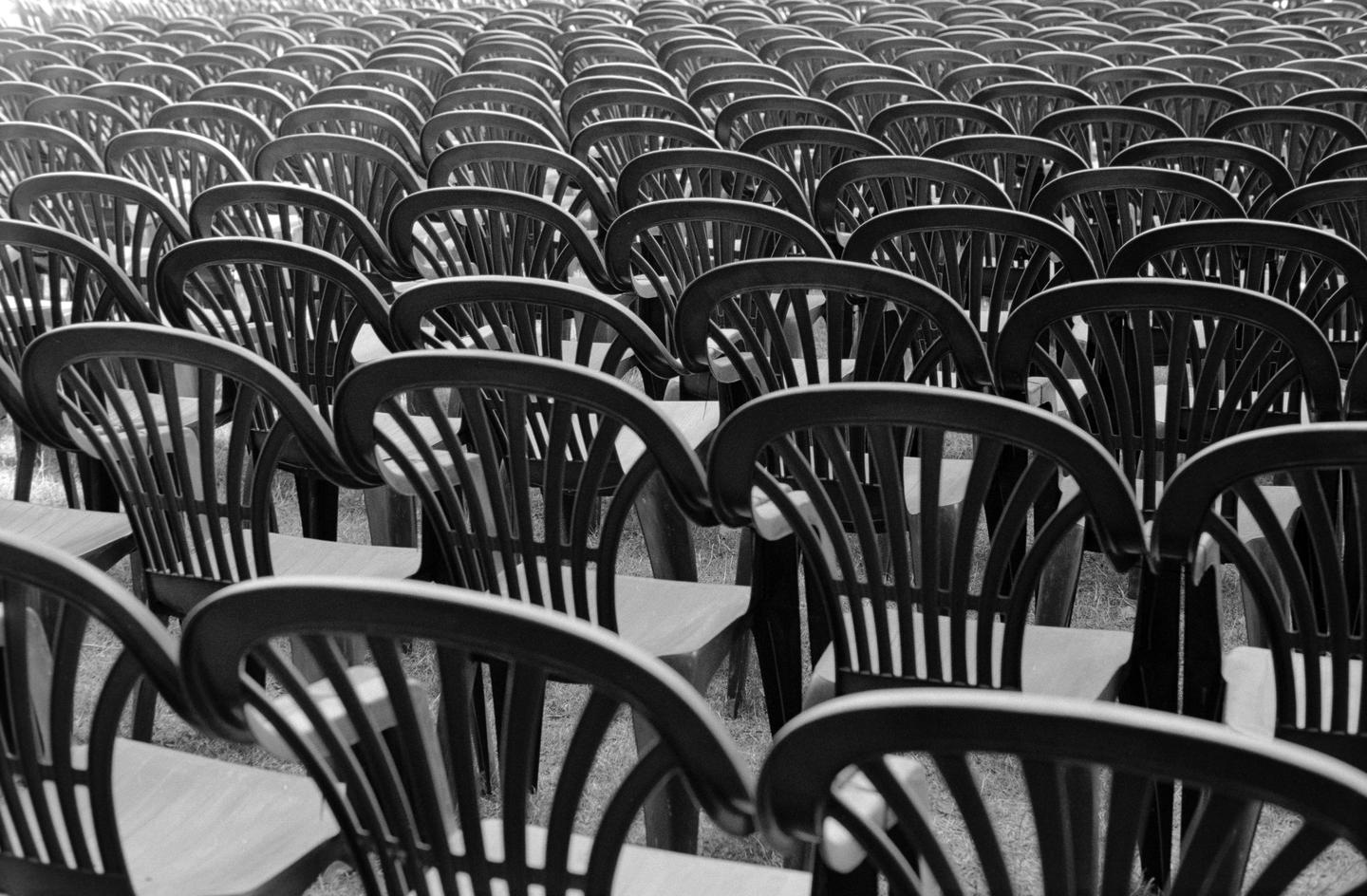 Many rows of empty chairs are arranged on a grassy field.