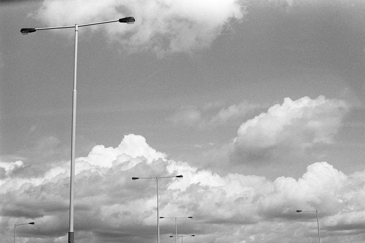 A tall street light stands against a cloudy sky, with several other street lights visible in the distance.