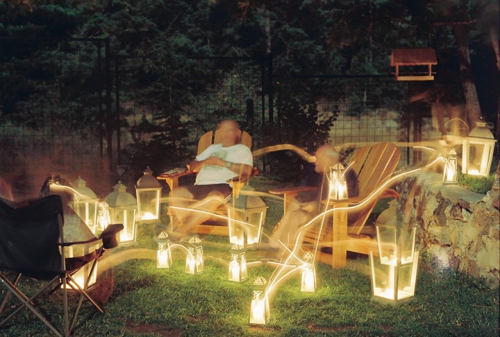 Two people sit in chairs surrounded by glowing lanterns and light trails at night.