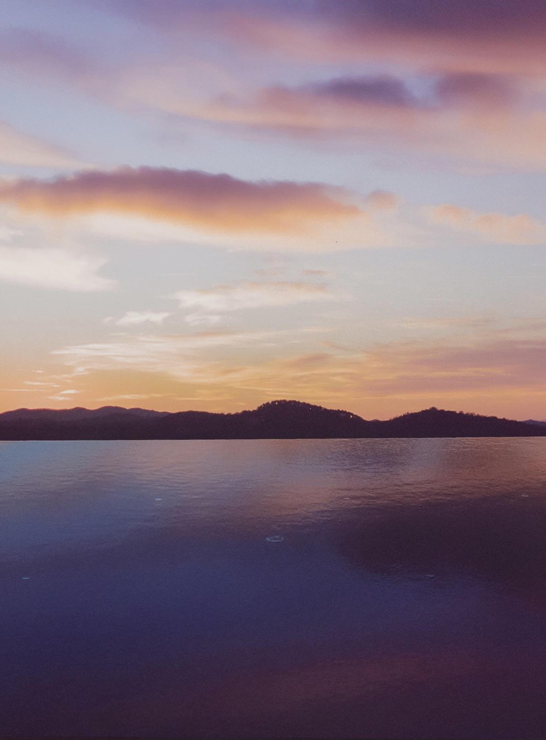 A body of water reflects the colorful sky and silhouetted hills at sunset.