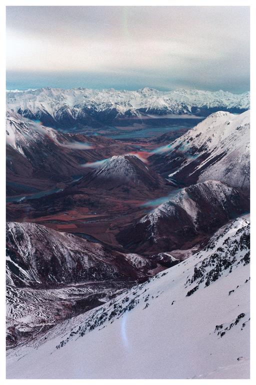 A vast mountain range with snow-capped peaks and a valley below is visible under a cloudy sky.