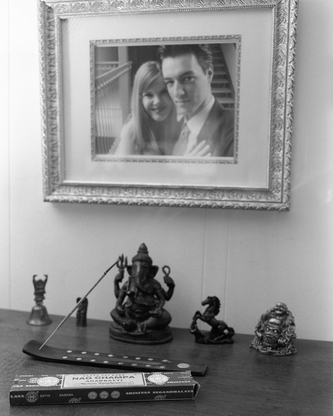 A framed black and white photograph of a couple is displayed above a wooden surface with various figurines and a box of incense.