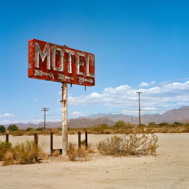 A weathered red motel sign stands in a desert landscape under a clear blue sky.