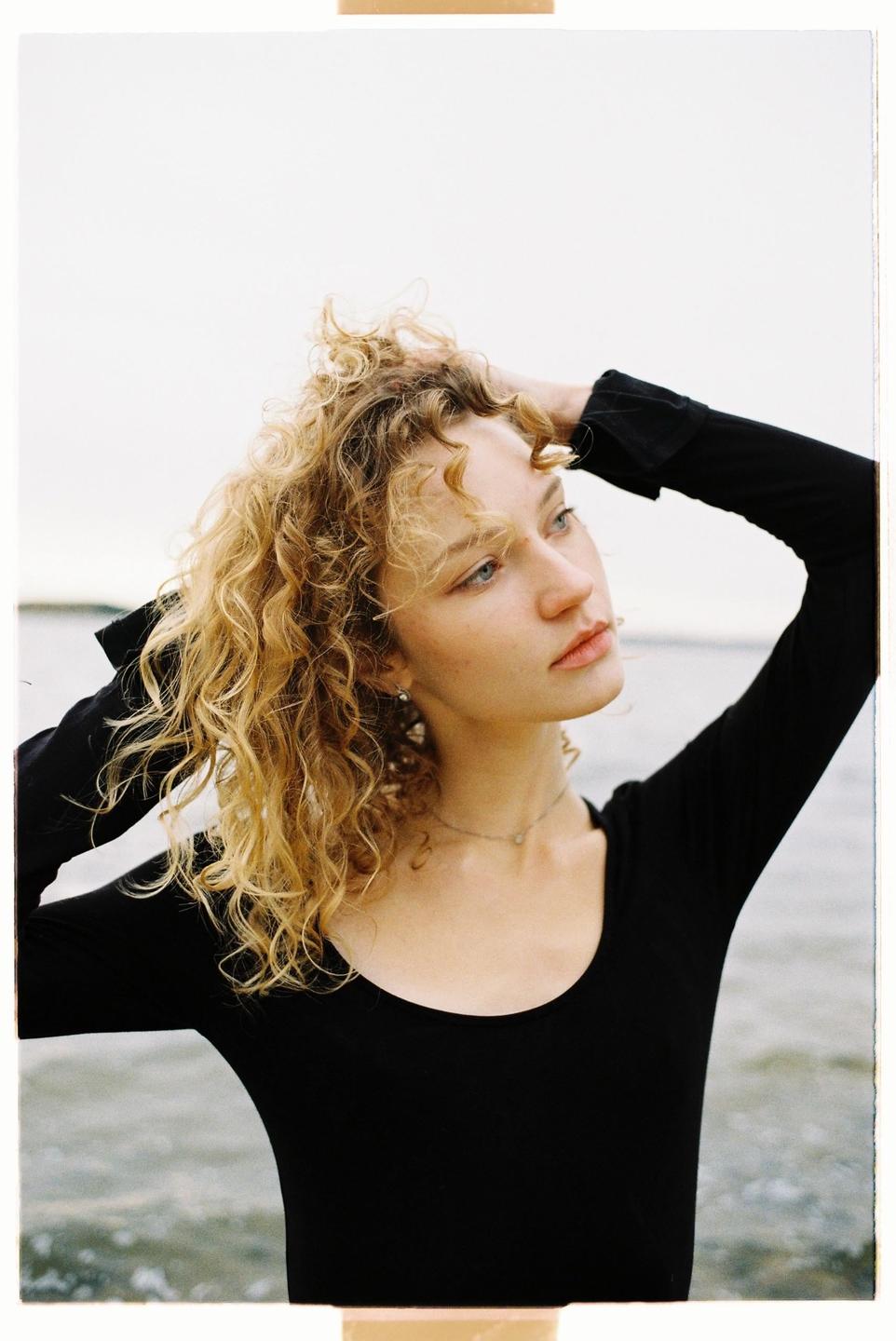 A woman with curly hair looks away from the camera with her hands in her hair.