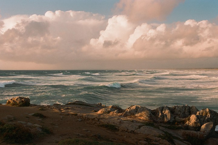 Waves crash against a rocky shore under a cloudy sky.
