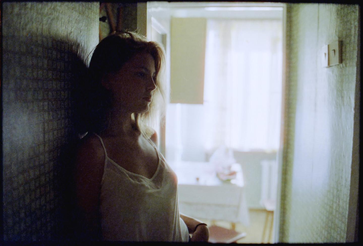 A woman stands in a doorway, looking towards a brightly lit room with a table.