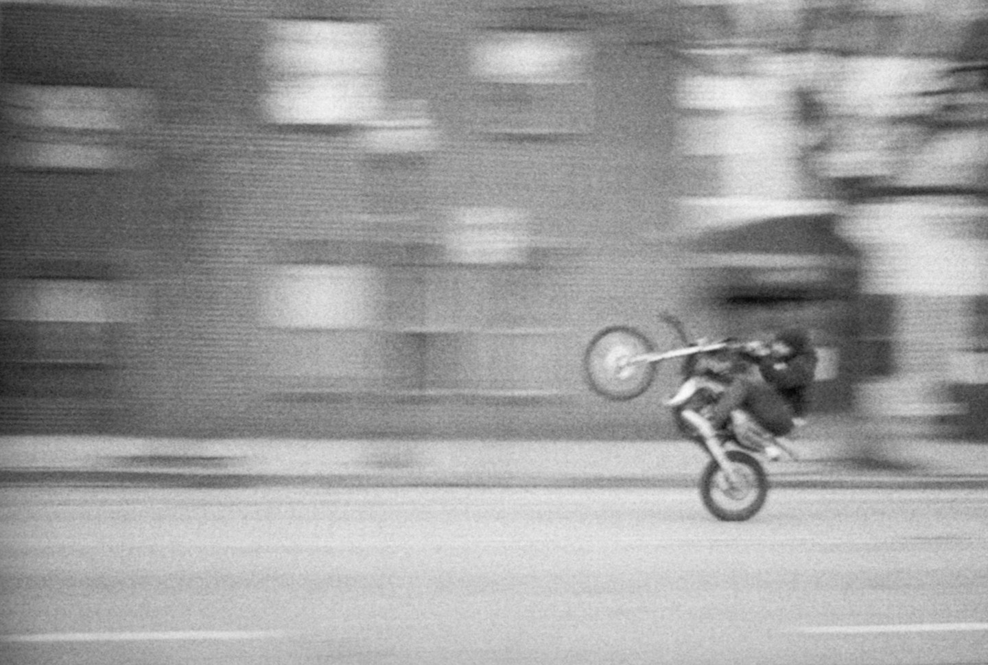 A person on a motorcycle performs a wheelie on a street in front of a building.