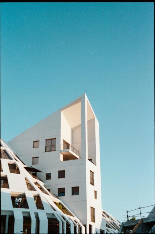A modern white building with a pointed roof and balconies stands against a clear blue sky.