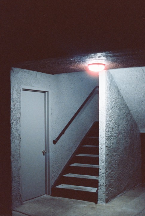 A red light illuminates a stairwell and a closed door at night.