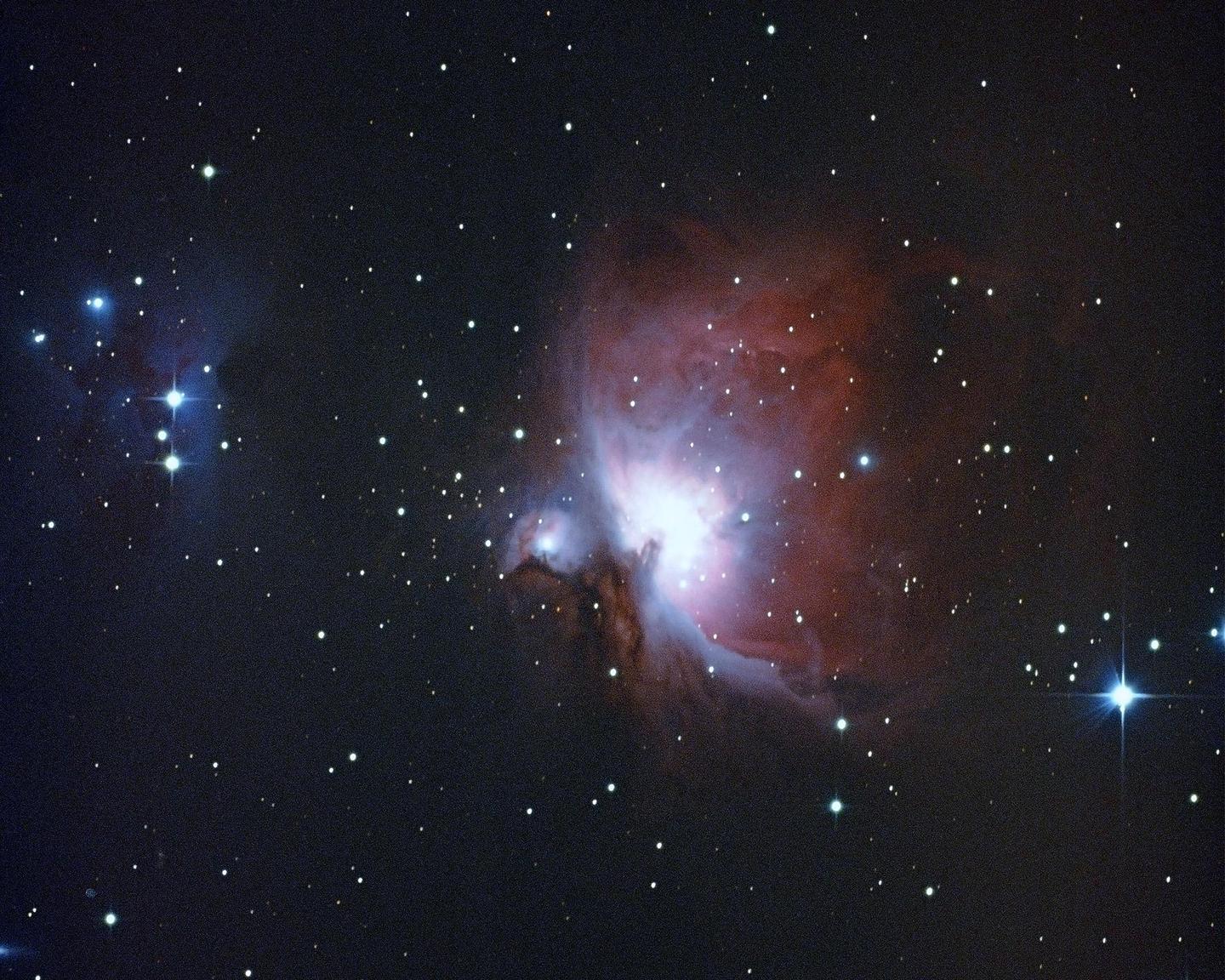 A bright nebula with red and blue hues is surrounded by numerous stars in a dark sky.