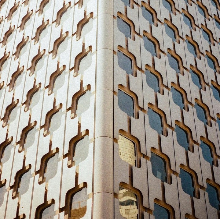 A building with a repeating pattern of windows and architectural details is shown from a low angle.