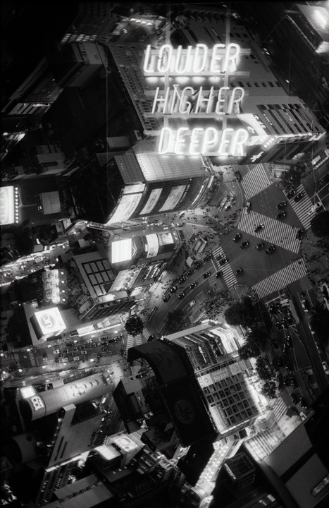 An aerial view of a city intersection at night shows buildings, cars, and pedestrians, with a neon sign reading "LOUDER HIGHER DEEPER" in a double exposure.