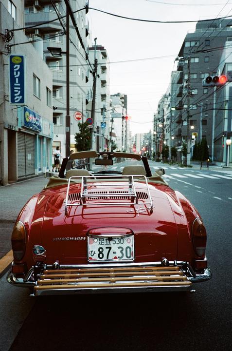 A red convertible car is parked on a city street lined with buildings and utility poles.