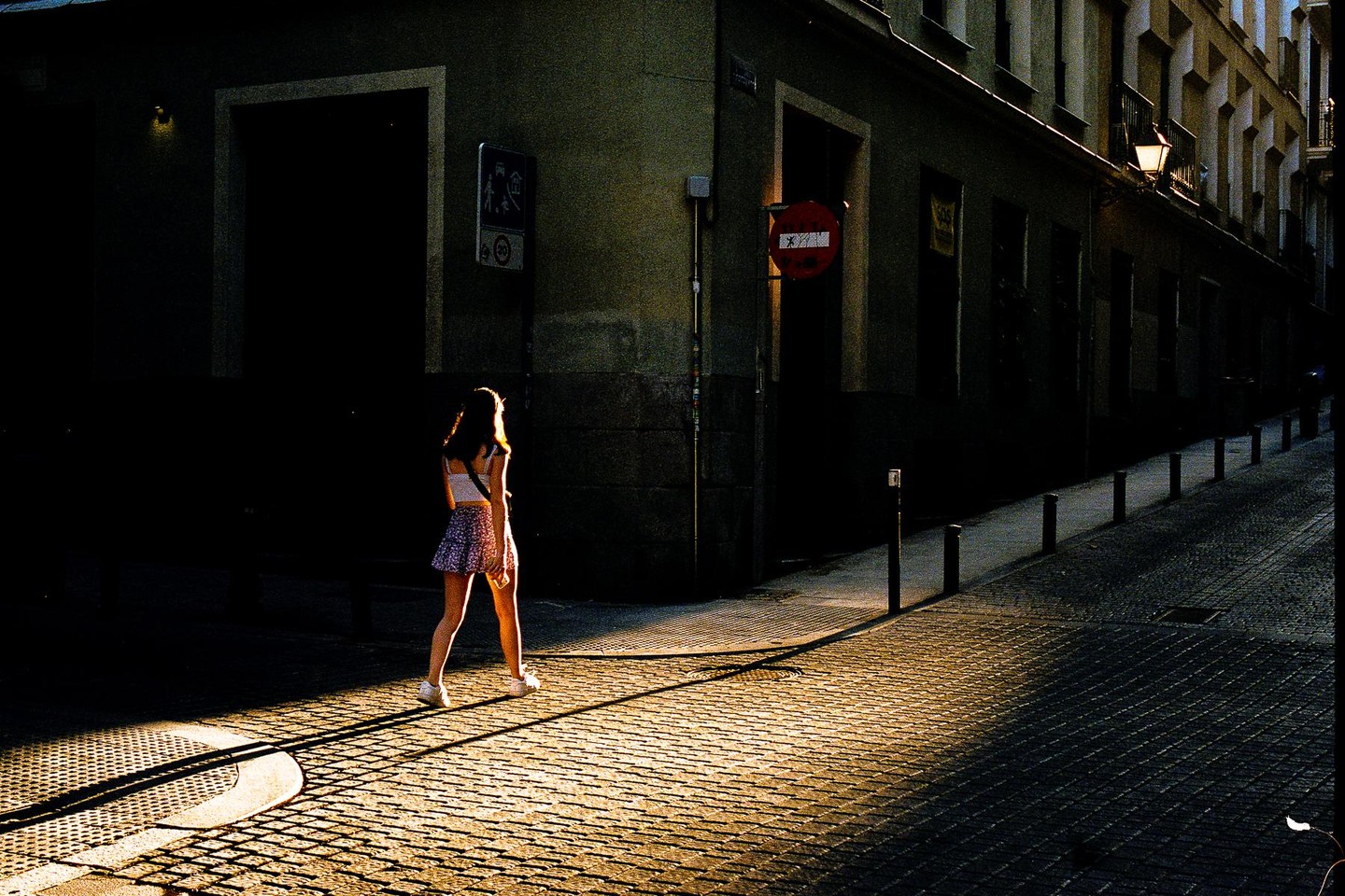 A woman walks on a cobblestone street in the evening light.