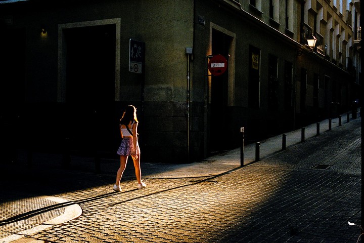 A woman walks on a cobblestone street in the evening light.