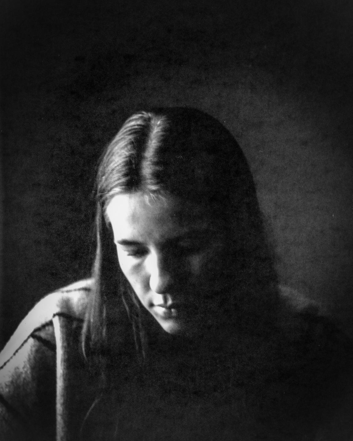 A woman with long hair looks down, her face partially illuminated by a soft light.