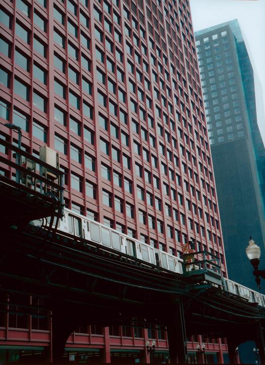 A train travels on an elevated track in front of a tall red building with many windows.
