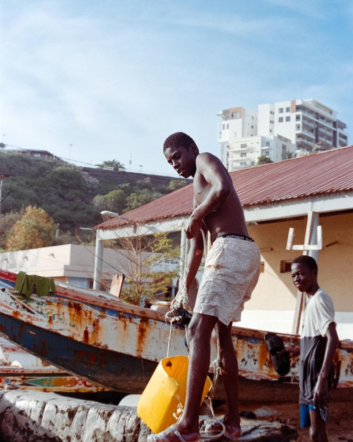 A boy stands on a boat and holds a yellow buoy while another boy stands behind him.
