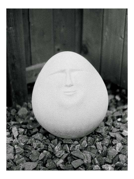 A round, smooth stone with a face carved into it rests on a bed of gravel.