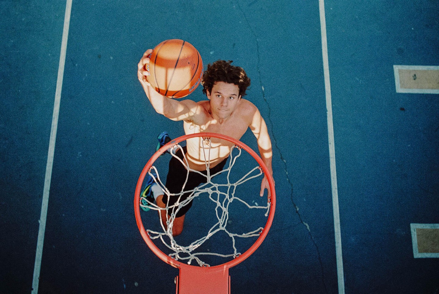A man dunks a basketball into a hoop on a blue court.