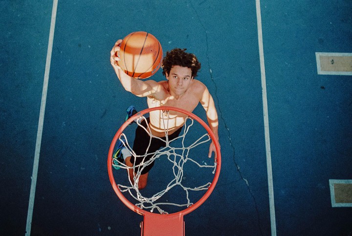 A man dunks a basketball into a hoop on a blue court.