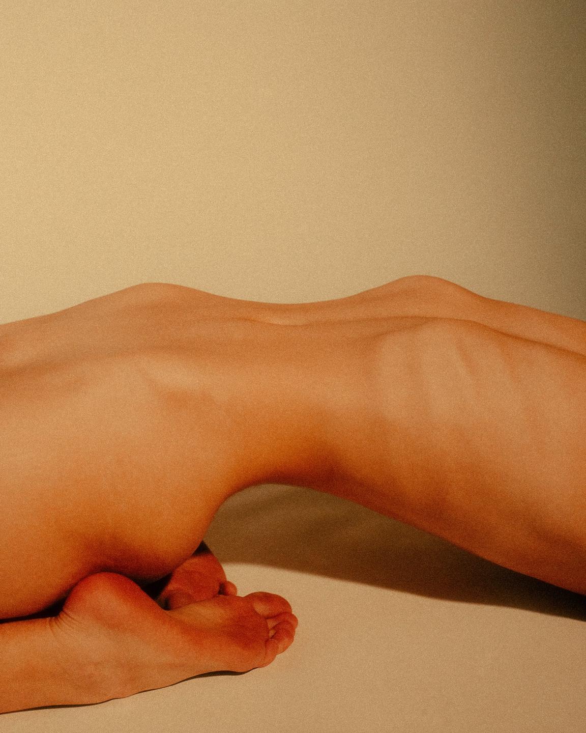 A person is lying on their stomach with their feet tucked under them, creating a silhouette against a light background.