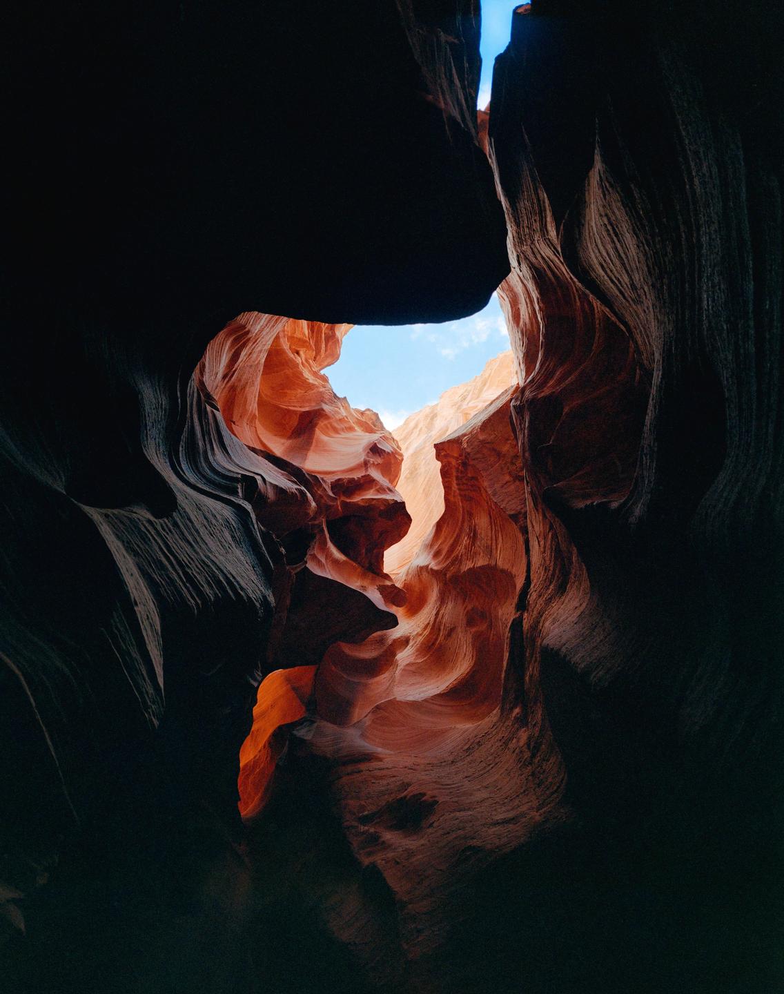 A narrow slot canyon with orange and red rock formations is illuminated by light from above.