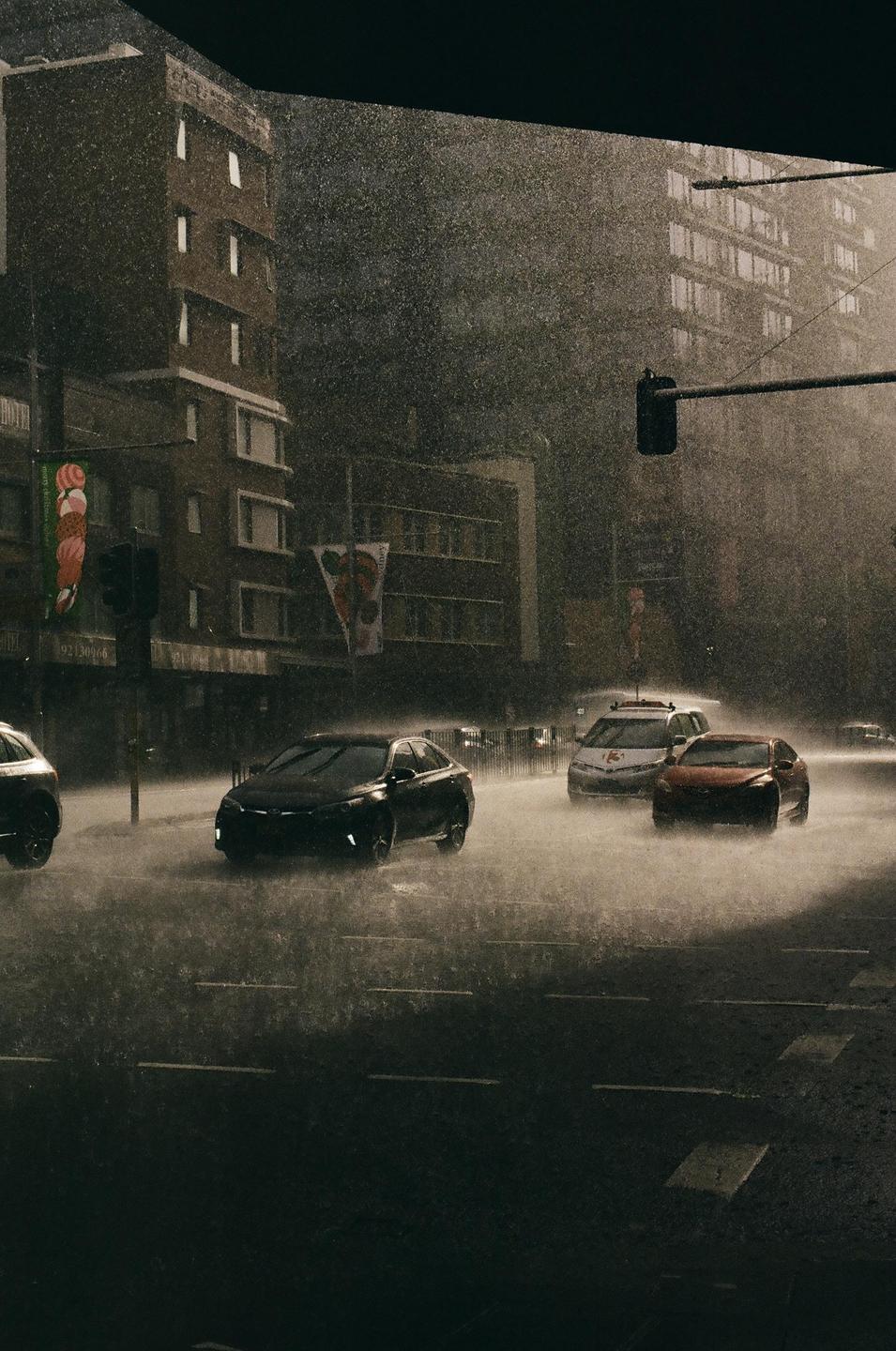 Cars drive through a city street during a sun shower.