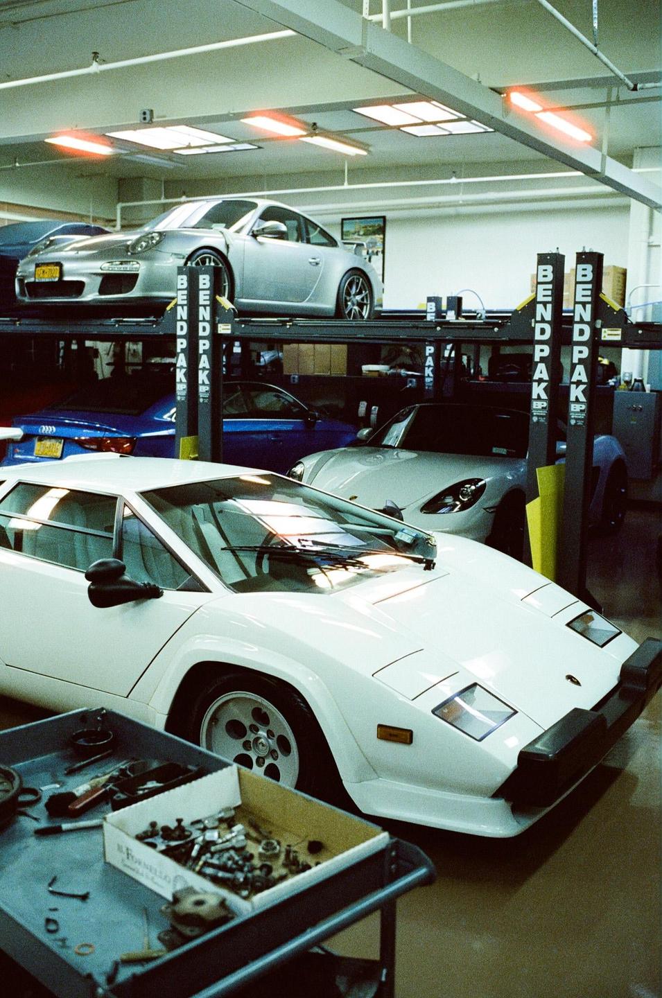 A white Lamborghini Countach is parked in a garage with other cars on lifts.