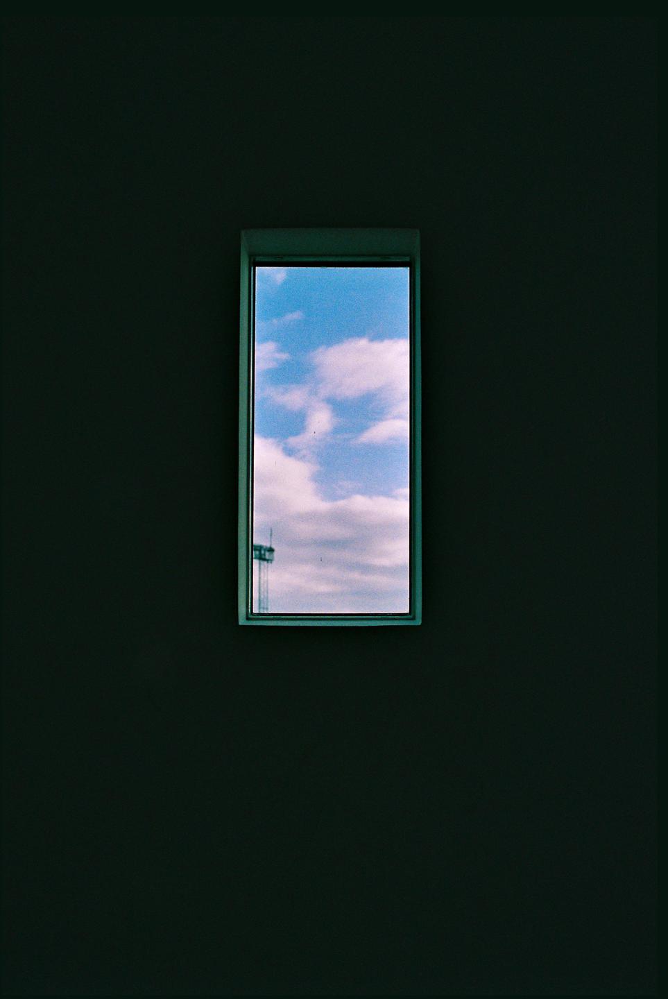 A small rectangular window shows a blue sky with white clouds and a distant structure.