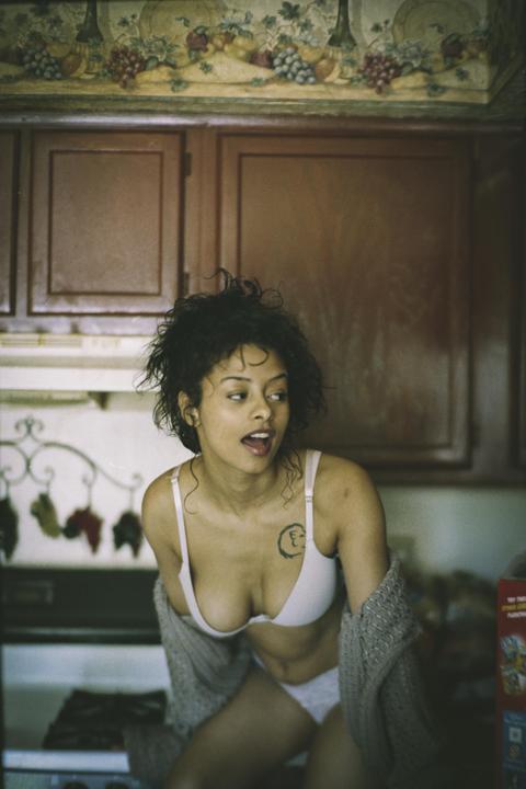 A woman in a bra and underwear looks to the side in a kitchen.