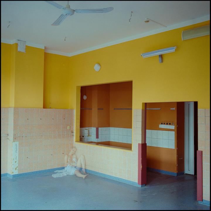 A ghostly figure of a woman sits on the floor of a room with yellow walls and tiled wainscoting.