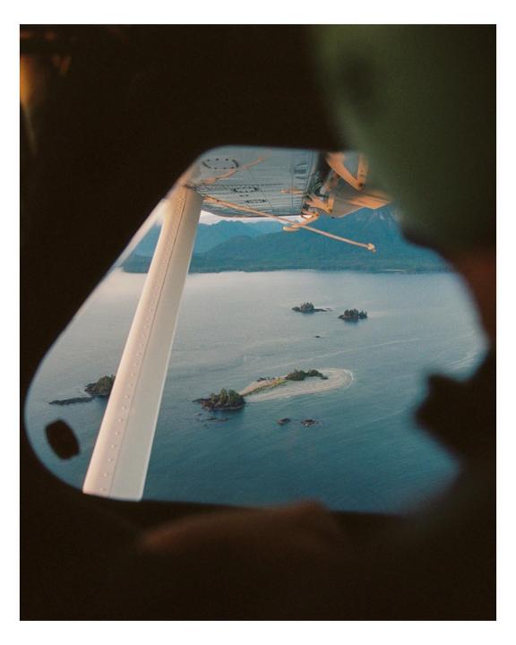 A view from a seaplane window shows small islands in a body of water with mountains in the distance.