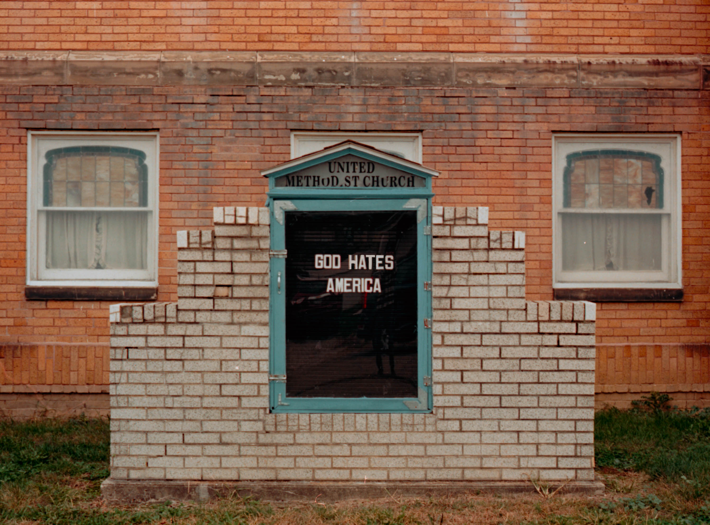 A brick church with a sign that reads "God Hates America" is visible.