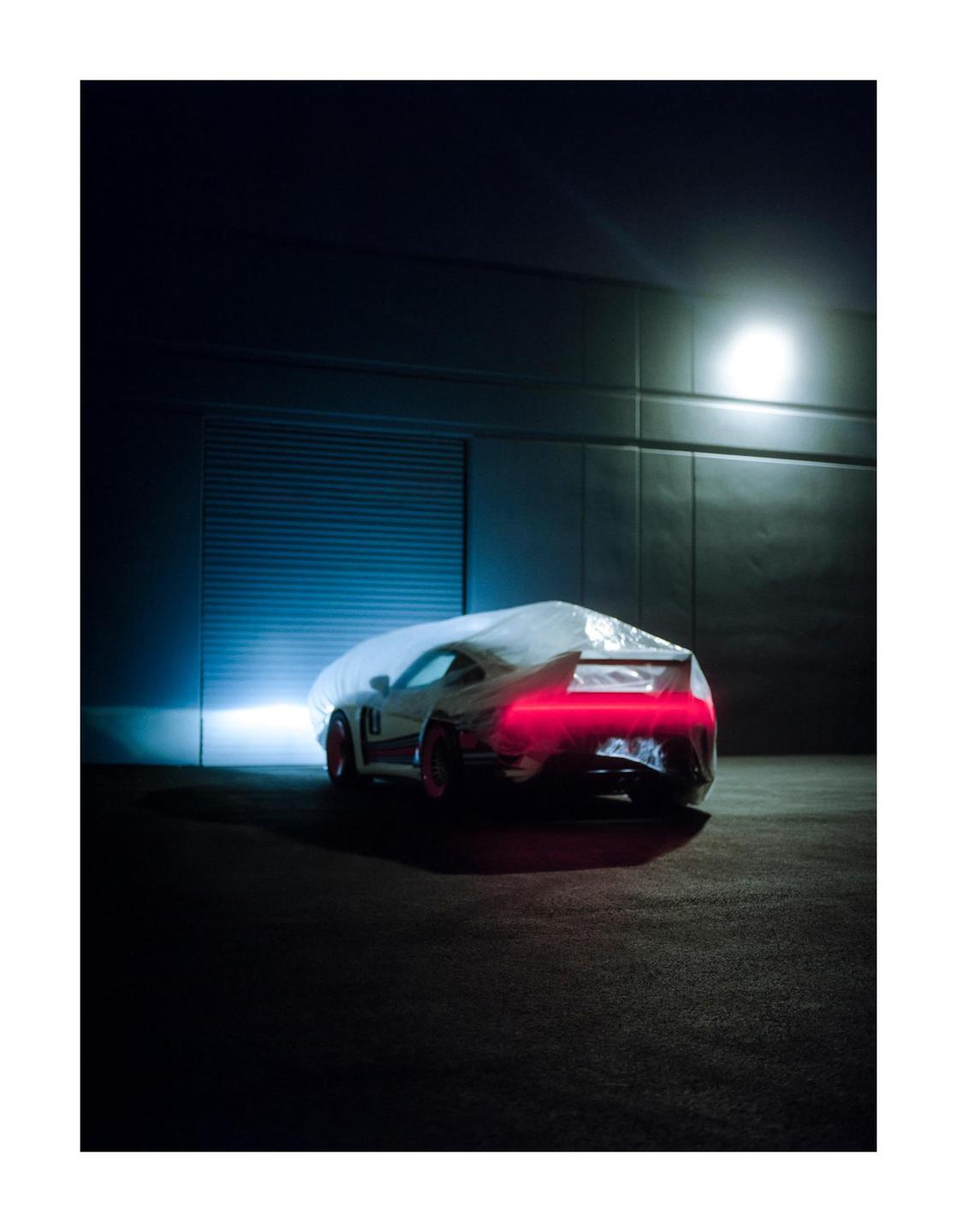 A car covered with a white sheet is parked in a dark garage with its red tail lights on.