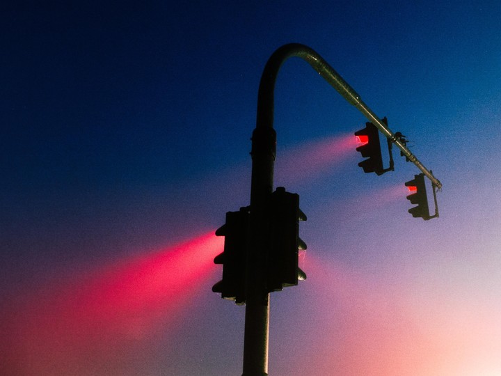 Three red traffic lights are illuminated against a gradient sky at dusk.